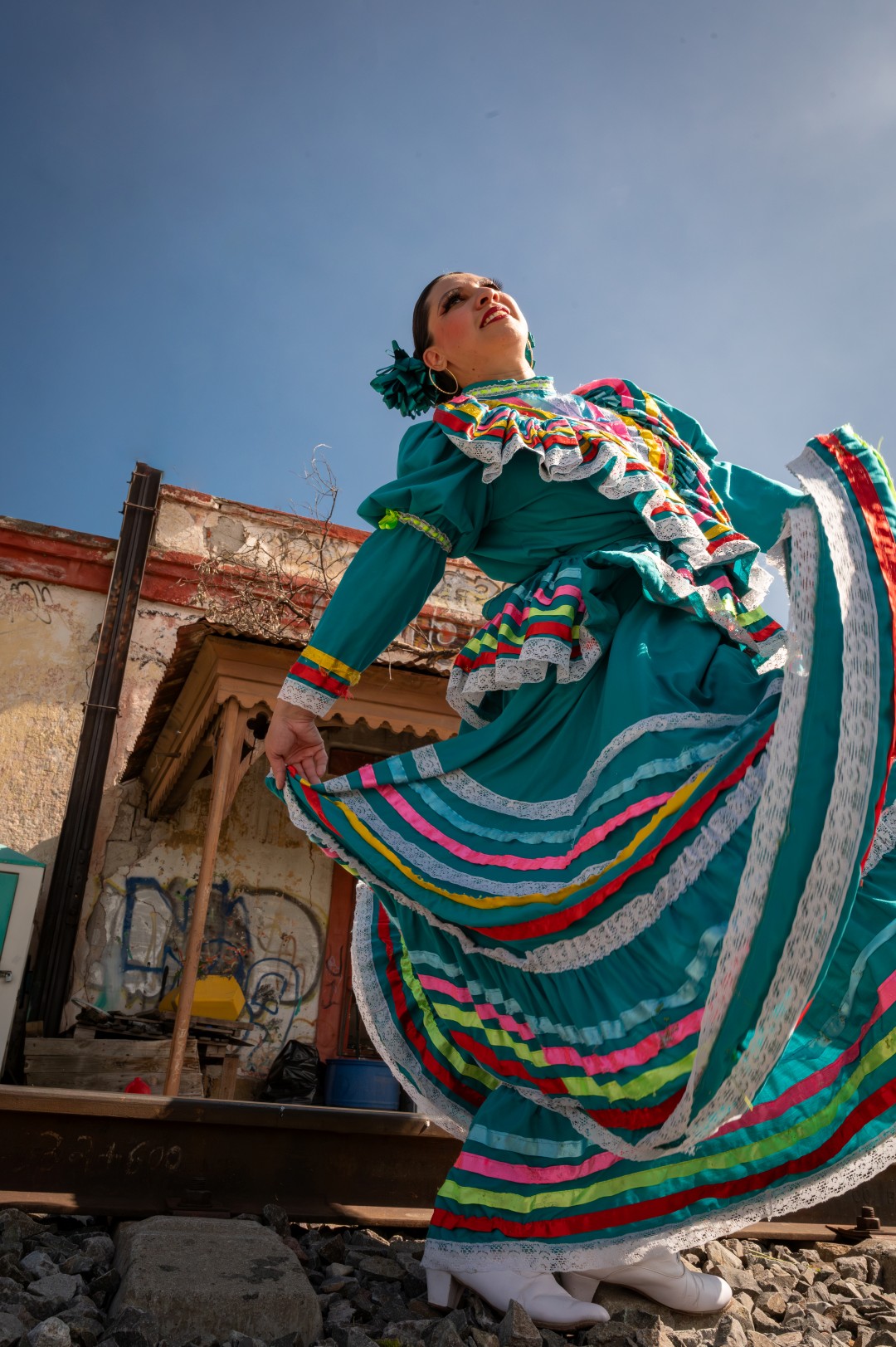 Artistic shot of a Mexican folkloric dancer in turquoise attire with rainbow ribbons,